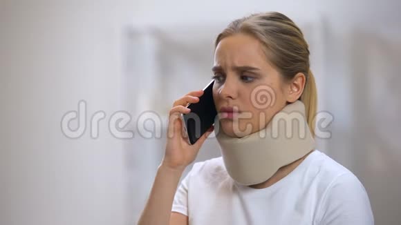 伤心的女人在泡沫颈项圈说话电话突然感觉到尖锐的颈部疼痛视频的预览图
