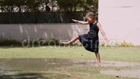 快乐的小女孩在草地上的水坑里跳做杂技轮视频的预览图