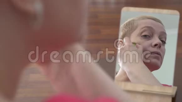一个相当成熟的女人在家里看着镜子用一片黄瓜搓着脸美容手术皮肤视频的预览图