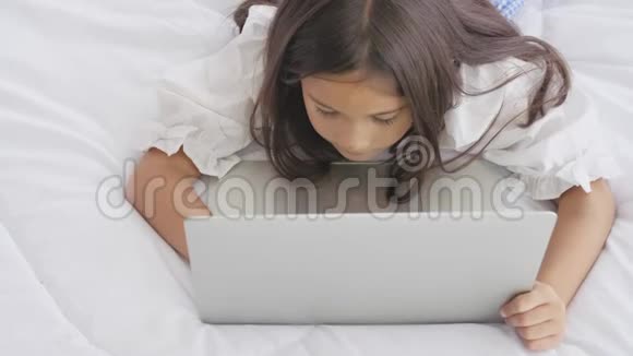可爱的白种人女孩躺在床上早上在家里的卧室里快乐地使用笔记本电脑技术和社会社区人民视频的预览图