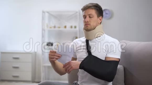 男人戴着泡沫颈项圈和手臂吊带阅读医疗账单价格惊人视频的预览图