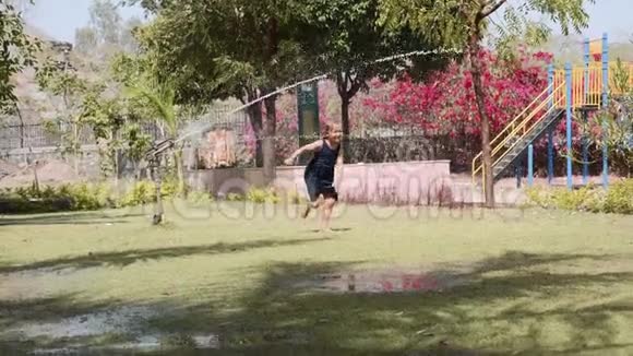 快乐女孩在儿童游乐场的草坪上的喷水管下奔跑视频的预览图
