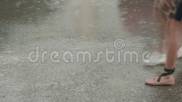 在夏雨之下女性的双腿在城市街道上的沥青路上行走两个女人在雨中走在潮湿的人行道上慢慢视频的预览图