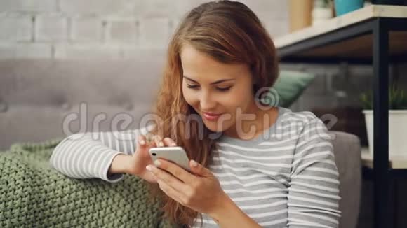 快乐的年轻女子手里拿着智能手机触摸屏幕微笑着查看社交媒体账户或阅读信息视频的预览图