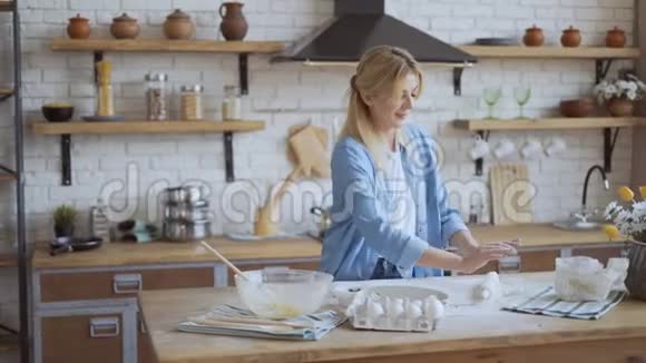 迷人的金发女人35岁在厨房里煮面团女人卷披萨面团4K视频的预览图