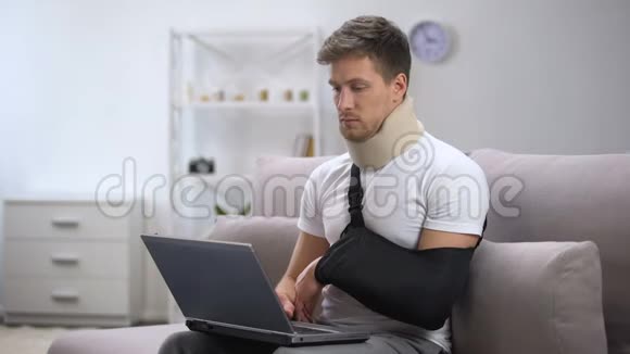 男性戴泡沫颈项圈和手臂吊带一只手在笔记本电脑上打字自由职业视频的预览图