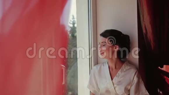 美丽美丽的女孩坐在窗台上把头从窗户转向相机微笑地看着相机视频的预览图