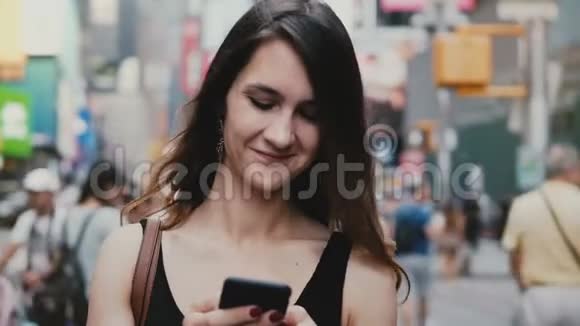 快乐轻松美丽的千禧女孩站在纽约街头用购物应用微笑看智能手机视频的预览图