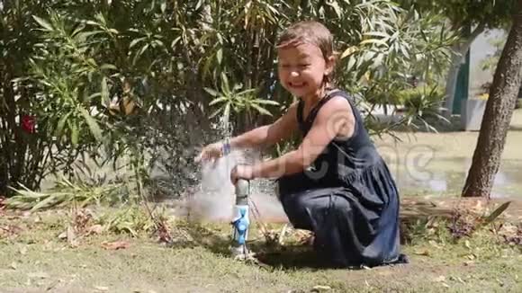 快乐的女孩在草地上玩水管上的喷水视频的预览图