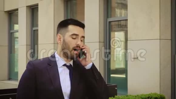 年轻的商人在办公楼中心附近的户外用手机聊天时感到很生气愤怒的男人视频的预览图