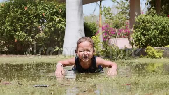 快乐的小女孩喜欢在公园的草坪上的水坑里泼水视频的预览图