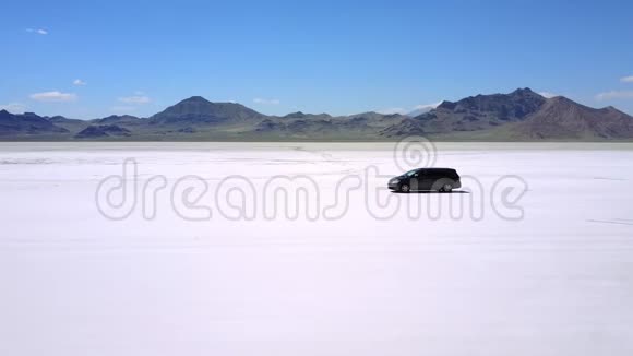 无人机跟随现代小型货车沿着平坦盐湖沙漠的大气景观进行完美的美国公路旅行视频的预览图