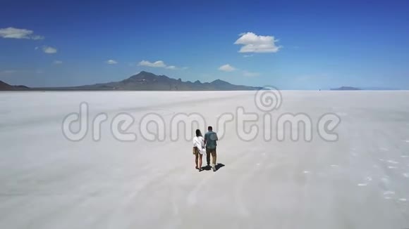 Drone跟着一对浪漫的情侣牵着手走向犹他州盐湖中心的白色平地视频的预览图