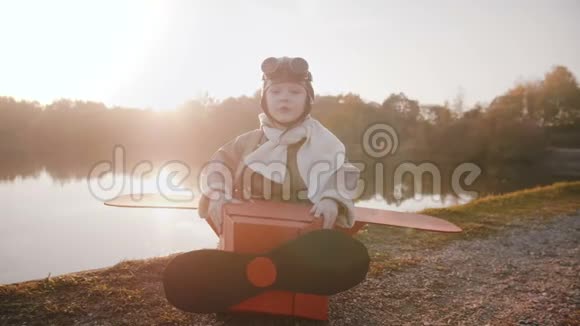 小快乐男孩穿着有趣的老飞机飞行员服装戴着航空眼镜在惊人的日落森林湖慢动作视频的预览图