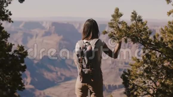 美丽的年轻快乐旅游女人带着背包看史诗般的大峡谷山脉走回镜头视频的预览图