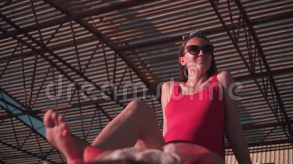 一个美丽的怀孕女孩穿着红色的一件泳衣和眼镜坐在一个阳光休息室视频的预览图