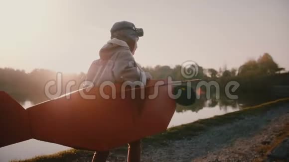 镜头跟随快乐的欧洲男孩沿着日落森林河奔跑玩飞机飞行员在有趣的服装慢动作视频的预览图