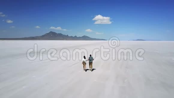 Drone跟着一对浪漫的情侣牵着手奔向史诗般的白色平坦的犹他州盐漠湖玩得很开心视频的预览图