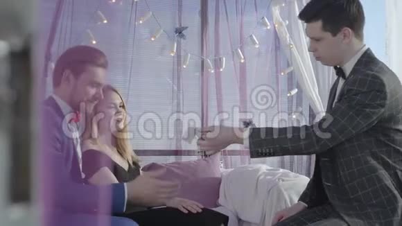 年轻快乐的大胡子男人把金发女人抱在沙发上魔术师为这对神奇的夫妇表演魔术视频的预览图