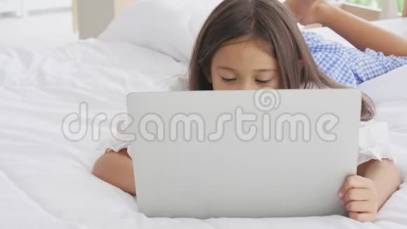 可爱的白种人女孩躺在床上早上在家里的卧室里快乐地使用笔记本电脑技术和社会社区人民视频的预览图