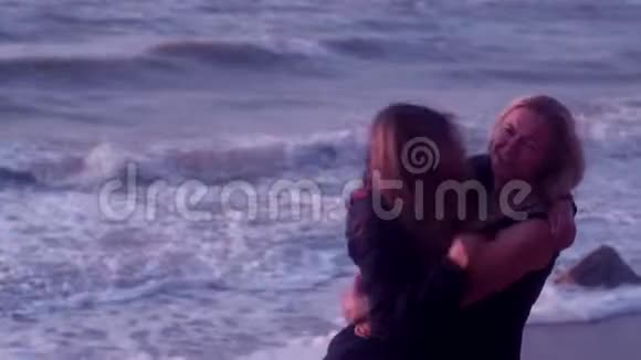妈妈和女儿拥抱欢笑微笑在大海巨浪泡沫海滩的背景下视频的预览图