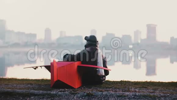 后景小飞行员女孩坐着有趣的红色纸板飞机在惊人的宁静的城市湖全景慢动作视频的预览图