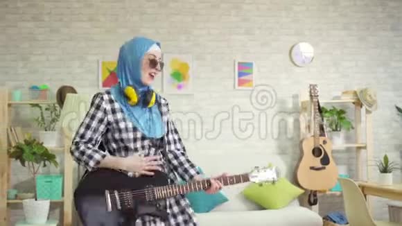 一位身穿头巾在家中弹电吉他的穆斯林年轻女子的肖像视频的预览图