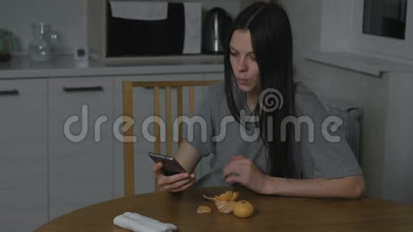 女人在电话里看一段有趣的视频晚上在厨房里吃橘子视频的预览图
