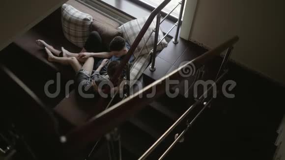 年轻漂亮的一对相爱的夫妇躺在客厅的沙发上靠近楼梯视频的预览图