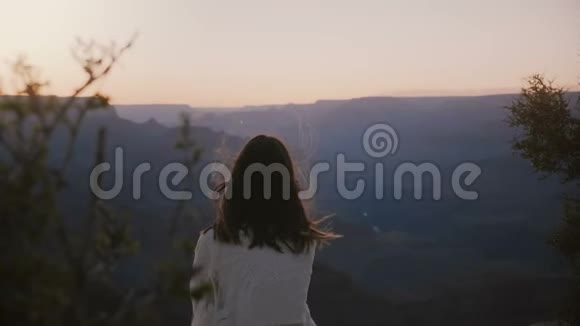 慢镜头后景快乐宁静的年轻女子飞扬的头发坐着观看史诗般的日落俯瞰大峡谷全景视频的预览图