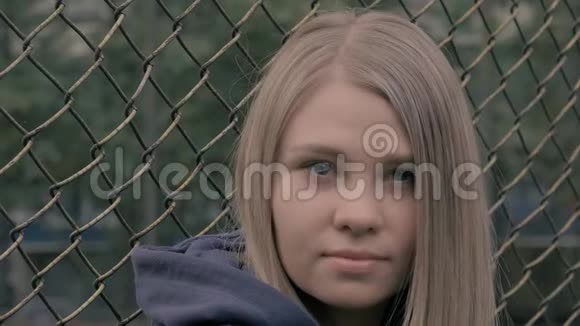 忧郁和悲伤的金发欧洲女孩的肖像背景是铁栅栏年轻女子仰头视频的预览图