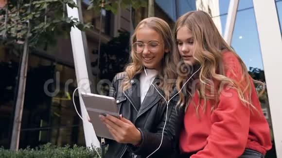 两位女性朋友在户外使用数码平板电脑微笑的女朋友看着平板电脑上的照片视频的预览图