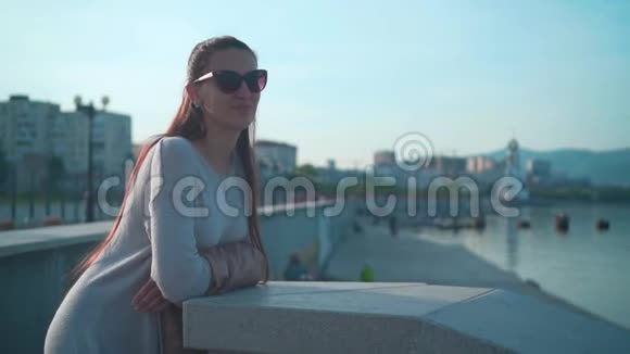 夏天天气晴朗戴太阳镜的年轻迷人女孩一个女孩站在靠近大海的堤岸上视频的预览图