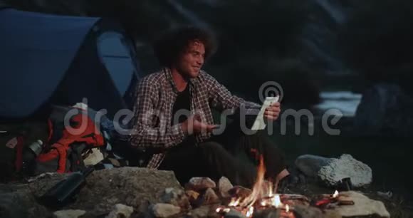 聊天时间用平板电脑在山中央露营年轻人在露营的时候有一个很棒的谈话在中间视频的预览图