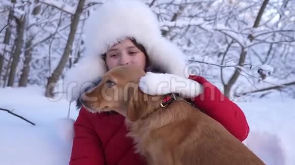 狗舔女孩脸美丽的女孩微笑抚摸她心爱的狗在公园冬天带着猎狗散步的女孩视频的预览图