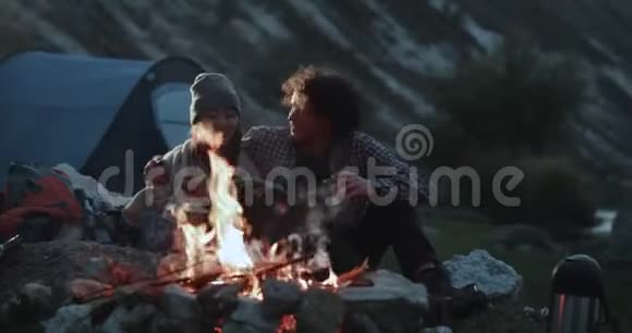 这对美丽的情侣在篝火旁喝着热饮互相拥抱共度浪漫时光视频的预览图