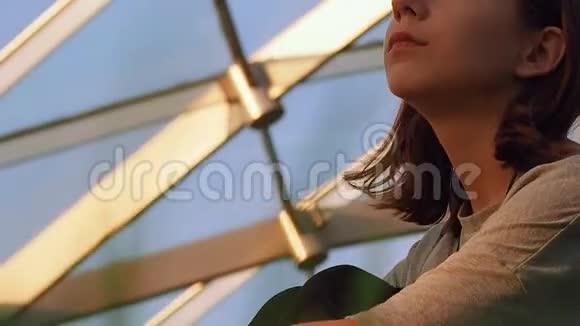 穿着灰色背心的贴身少女坐在穹顶下的一个公园里晚上在灯光的照射下环顾四周视频的预览图