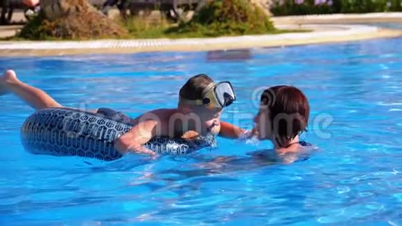 幸福的家庭妈妈和小儿子围成一个圆圈在酒店的游泳池里用蓝色的水游泳慢动作视频的预览图