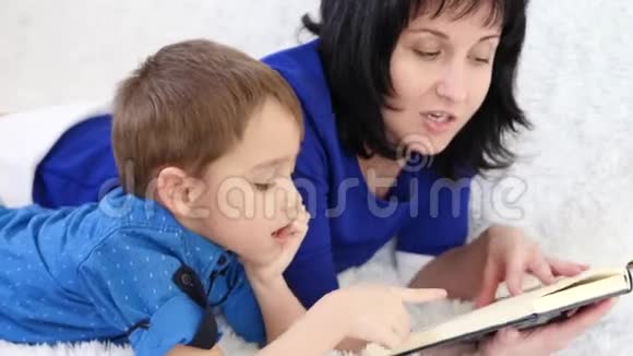 快乐的妈妈和她的孩子正在看一本躺在白色沙发上的书视频的预览图