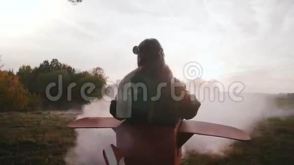 小微笑的飞行员女孩在有趣的纸板飞机旋转与彩色烟雾在美丽的日落场慢动作视频的预览图