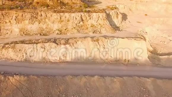 在一个阳光明媚的日子里一个赤脚的年轻女人沿着一个又大又深的沙坑的尘土飞扬的道路行走空中景观视频的预览图