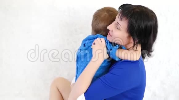 年轻的黑发母亲把儿子抱在白色沙发上幸福家庭的概念视频的预览图