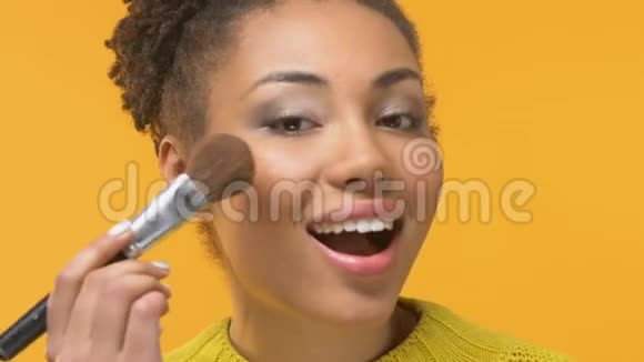 微笑的非洲女人用化妆刷美容趋势时尚视频的预览图