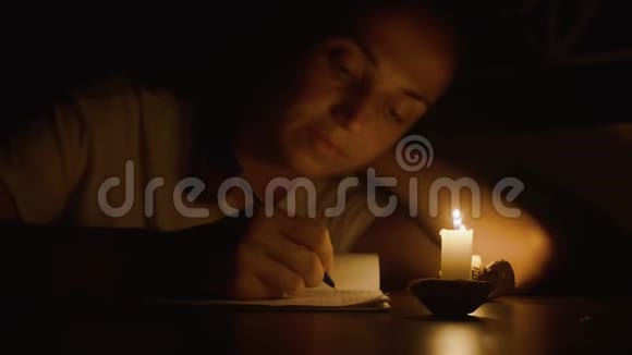在昏暗的房间里年轻女子正在烛光下用笔写字视频的预览图