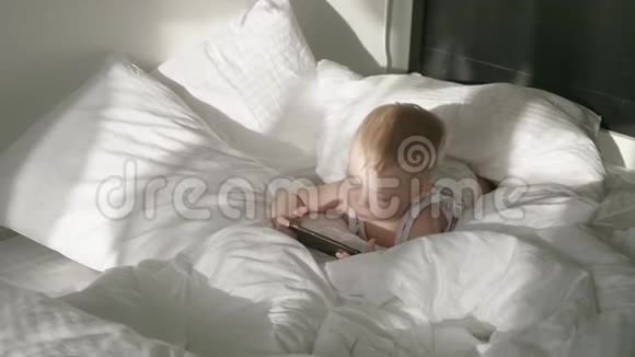 小男孩在家里的床上看智能手机上的卡通生活方式视频的预览图