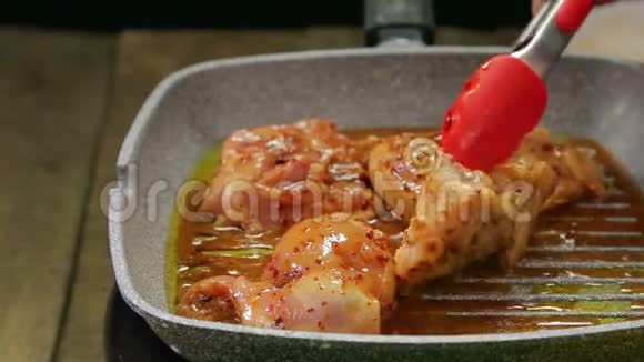 一个女人的手烤盘上用钳子把鸡肉翻过来把酱汁倒在上面视频的预览图