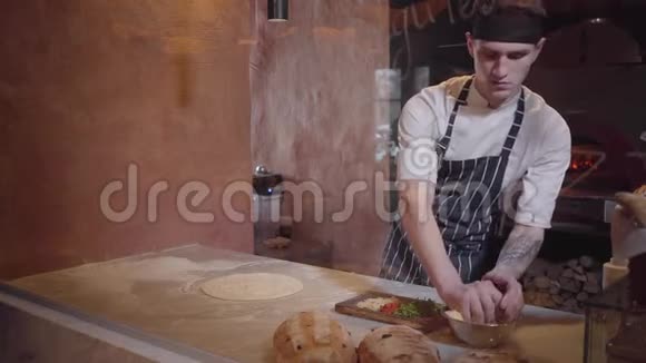 熟练的披萨制造商正在玻璃后面的现代餐厅厨房做面团他把比萨饼的原料视频的预览图