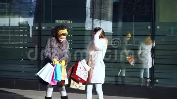 两个手里拿着东西的女孩站在商店橱窗附近的街道上视频的预览图