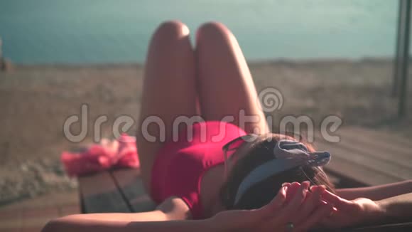 一个美丽的怀孕女孩穿着红色的一件泳衣和眼镜坐在一个阳光休息室视频的预览图