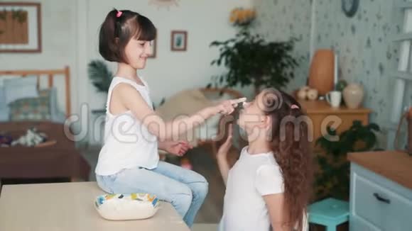 可爱的女孩用面粉涂抹姐姐的脸在厨房里玩得开心动作慢视频的预览图